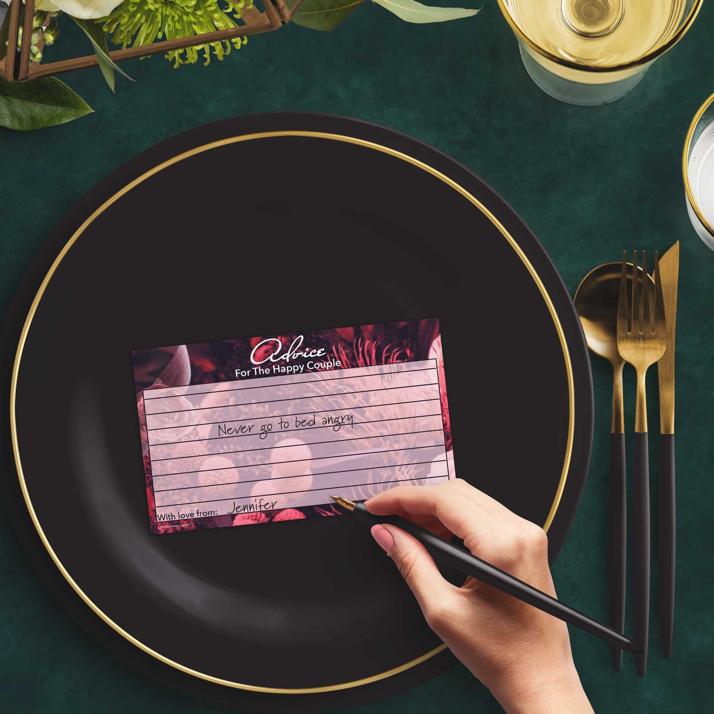 Woman with a pen sitting at a dark place setting with a black and gold plate filling out a dark floral Advice for the Happy Couple card