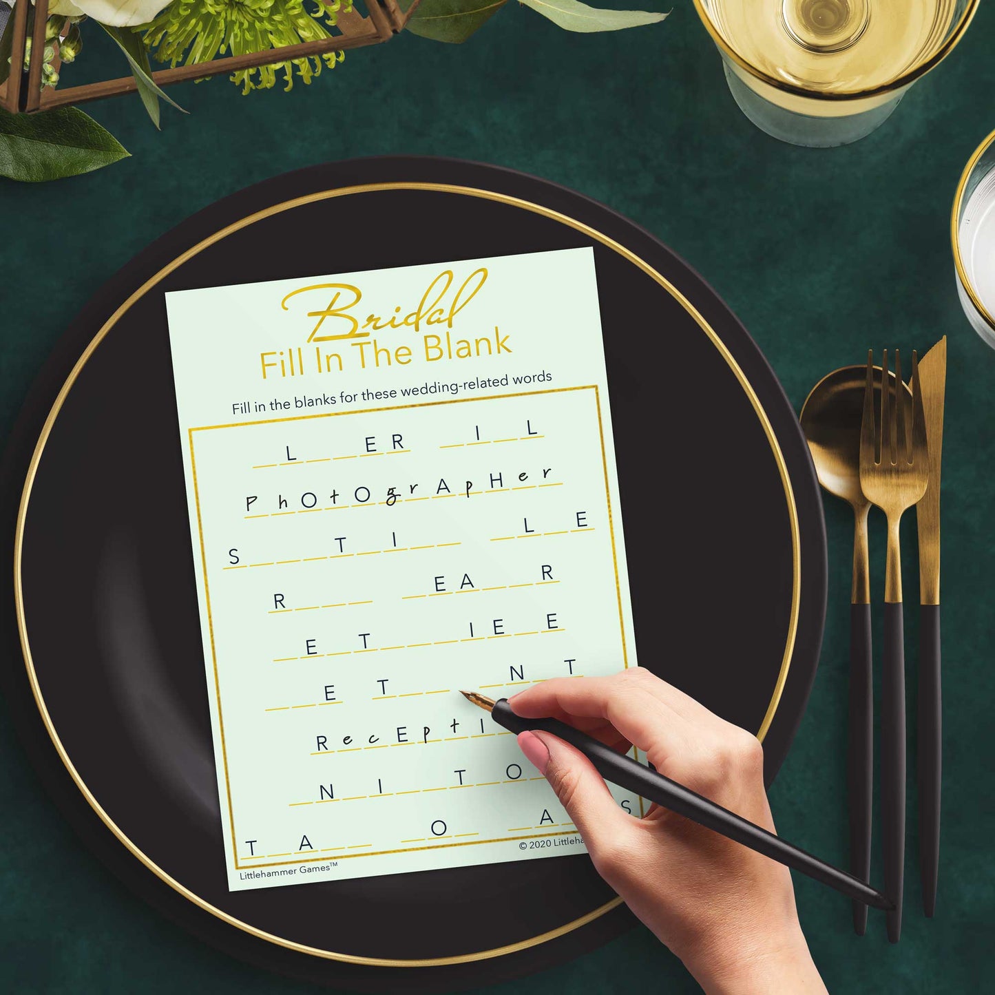 Woman with a pen playing a mint and gold Bridal Fill in the Blank game card at a dark place setting