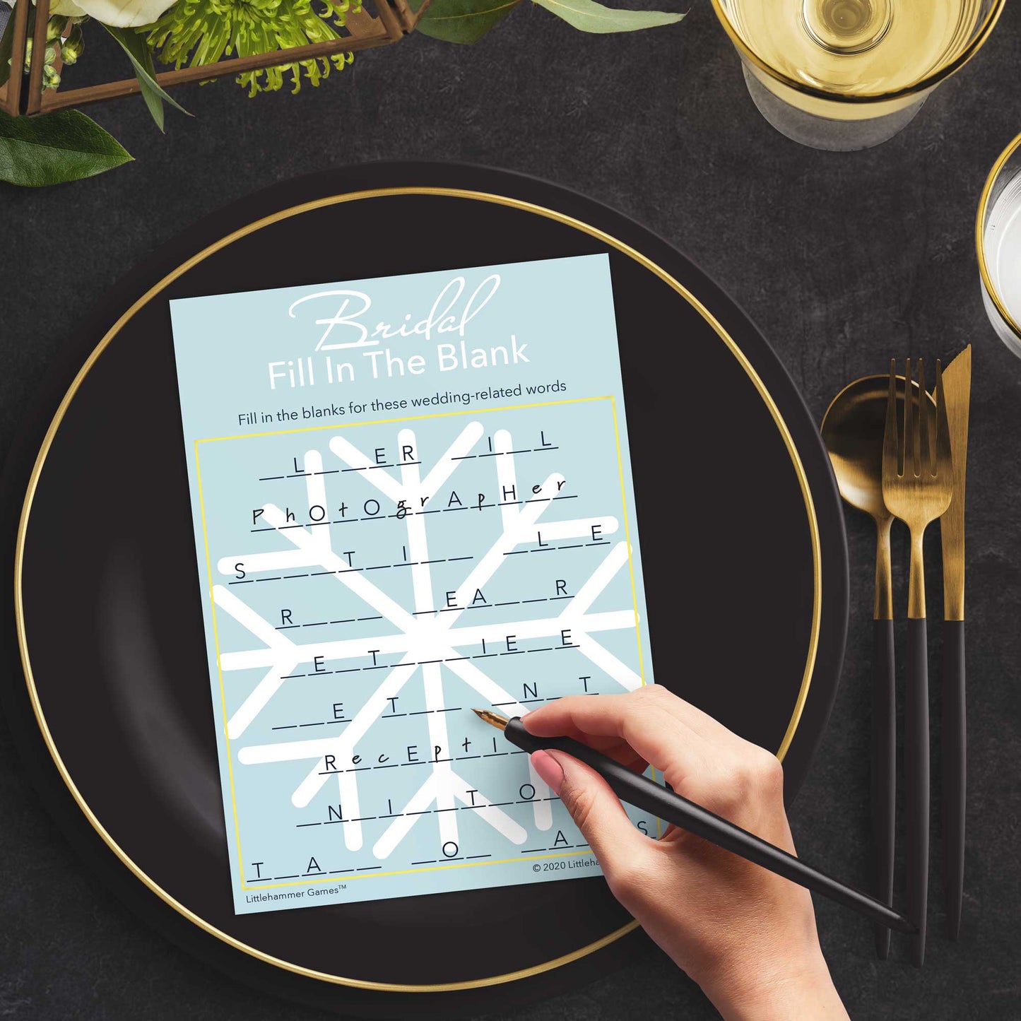 Woman with a pen playing a snowflake Bridal Fill in the Blank game card at a dark place setting