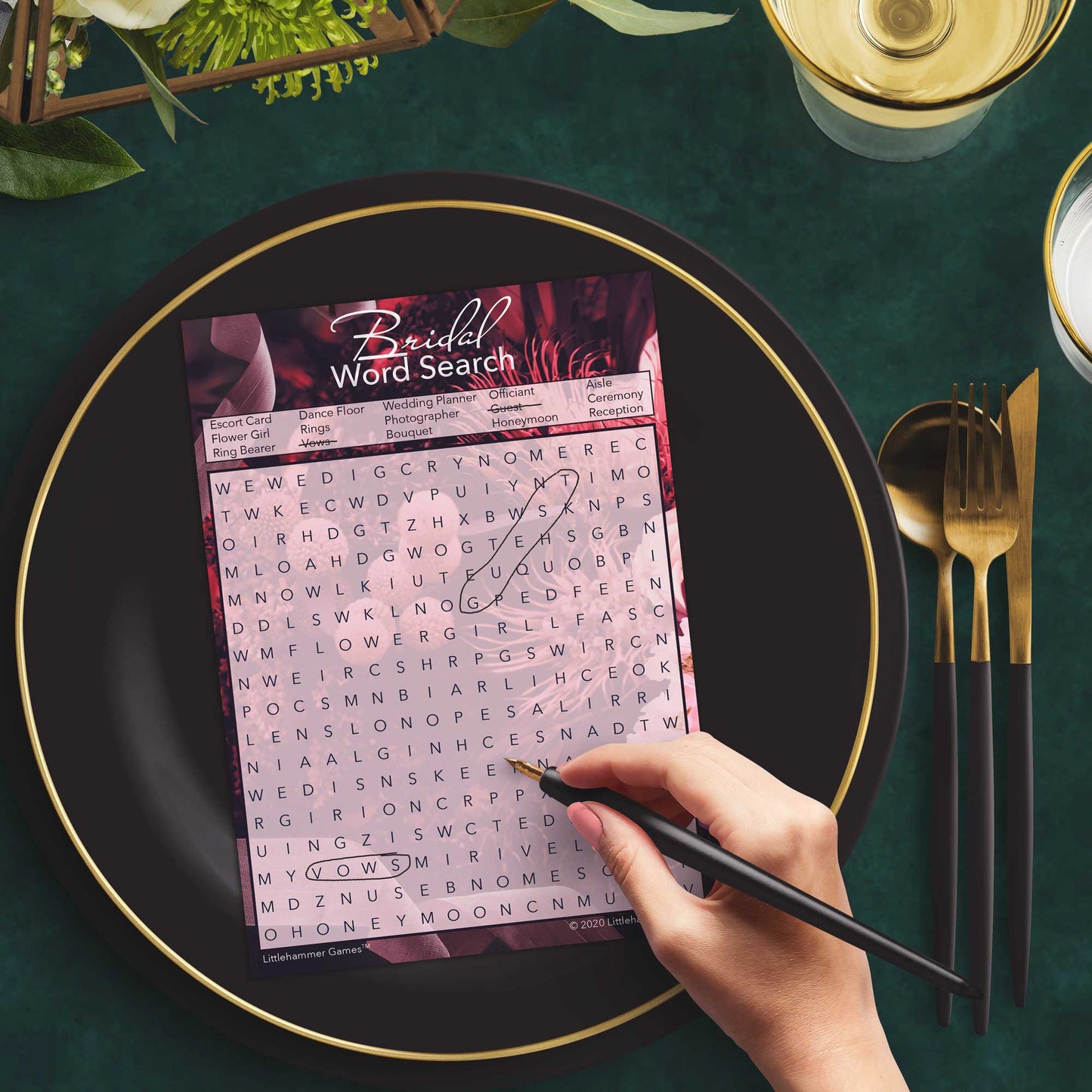 Woman with a pen playing a dark floral Bridal Word Search game card at a dark place setting