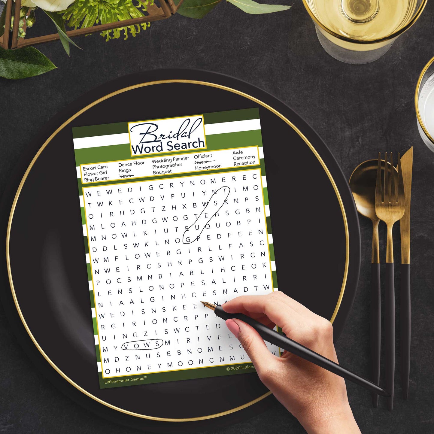 Woman with a pen playing a green-striped Bridal Word Search game card at a dark place setting
