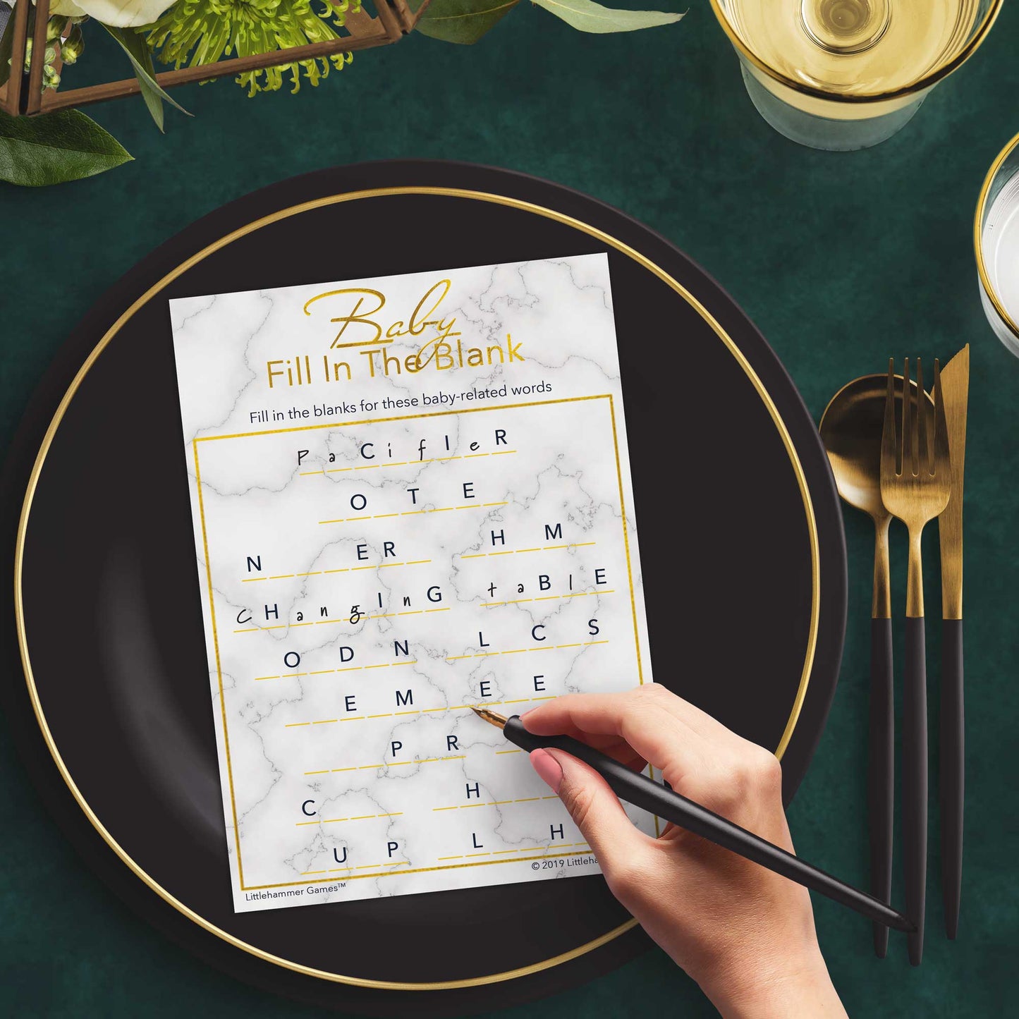Woman with a pen playing a gold and marble Baby Fill in the Blank game card at a dark place setting