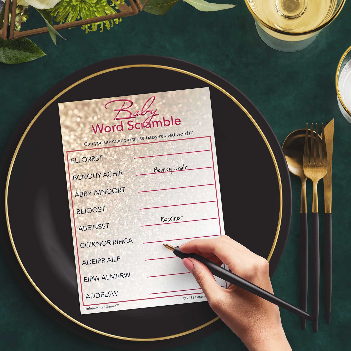 Woman playing a glittery rose gold Baby Word Scramble game card at a green and black place setting