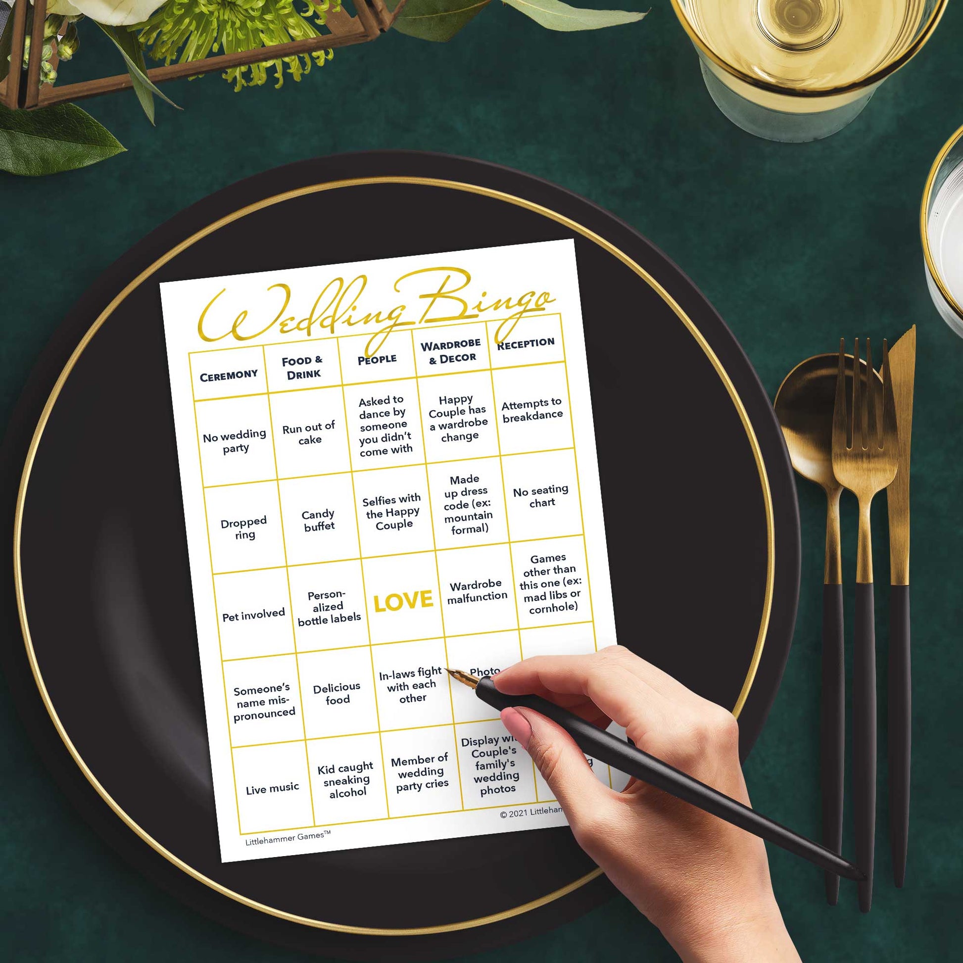 Woman with a pen sitting at a table with a gold and white Wedding Bingo game card on a black and gold plate at a dark place setting