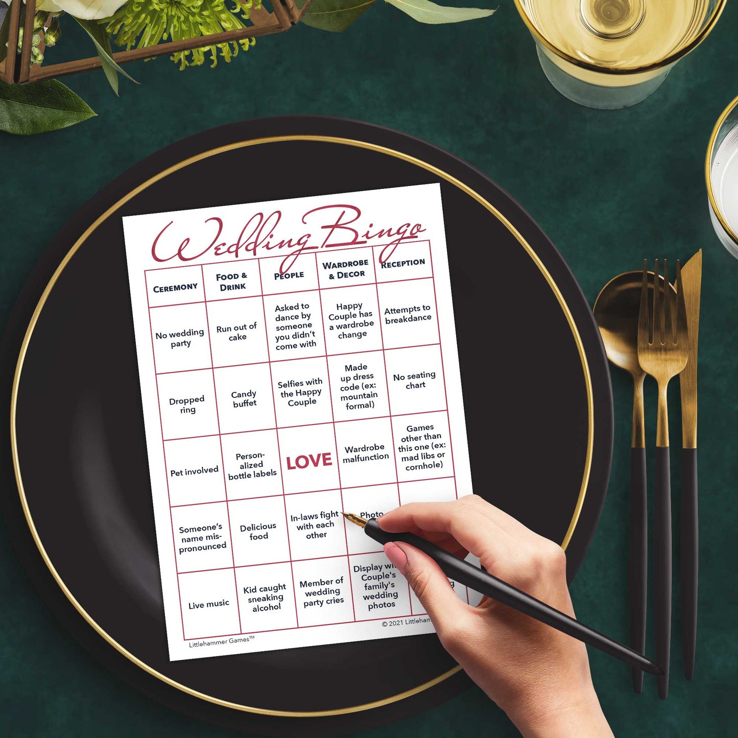 Woman with a pen sitting at a table with a rose gold and white Wedding Bingo game card on a black and gold plate at a dark place setting