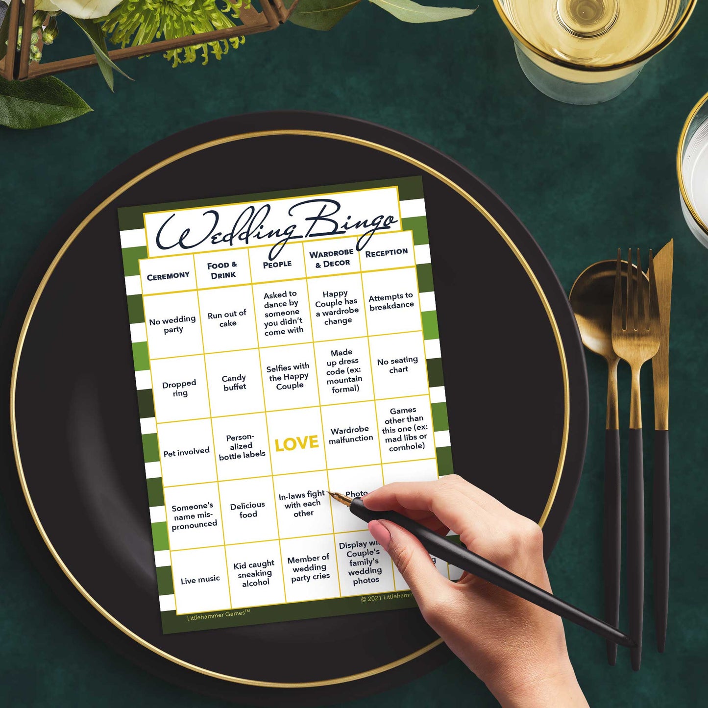 Woman with a pen sitting at a table with a green-striped Wedding Bingo game card on a black and gold plate at a dark place setting