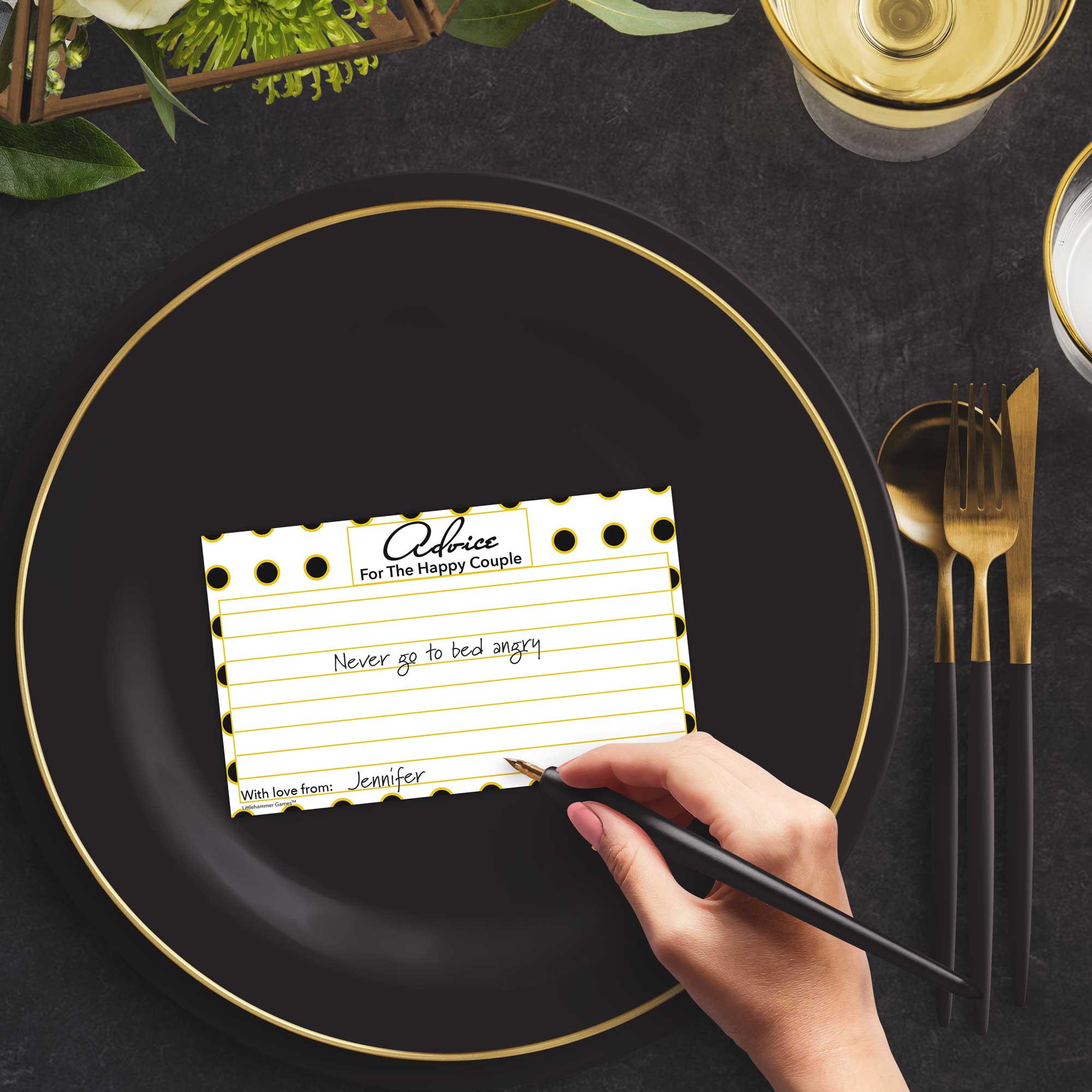 Woman with a pen sitting at a dark place setting with a black and gold plate filling out a black and gold polka dot advice for the newlyweds card