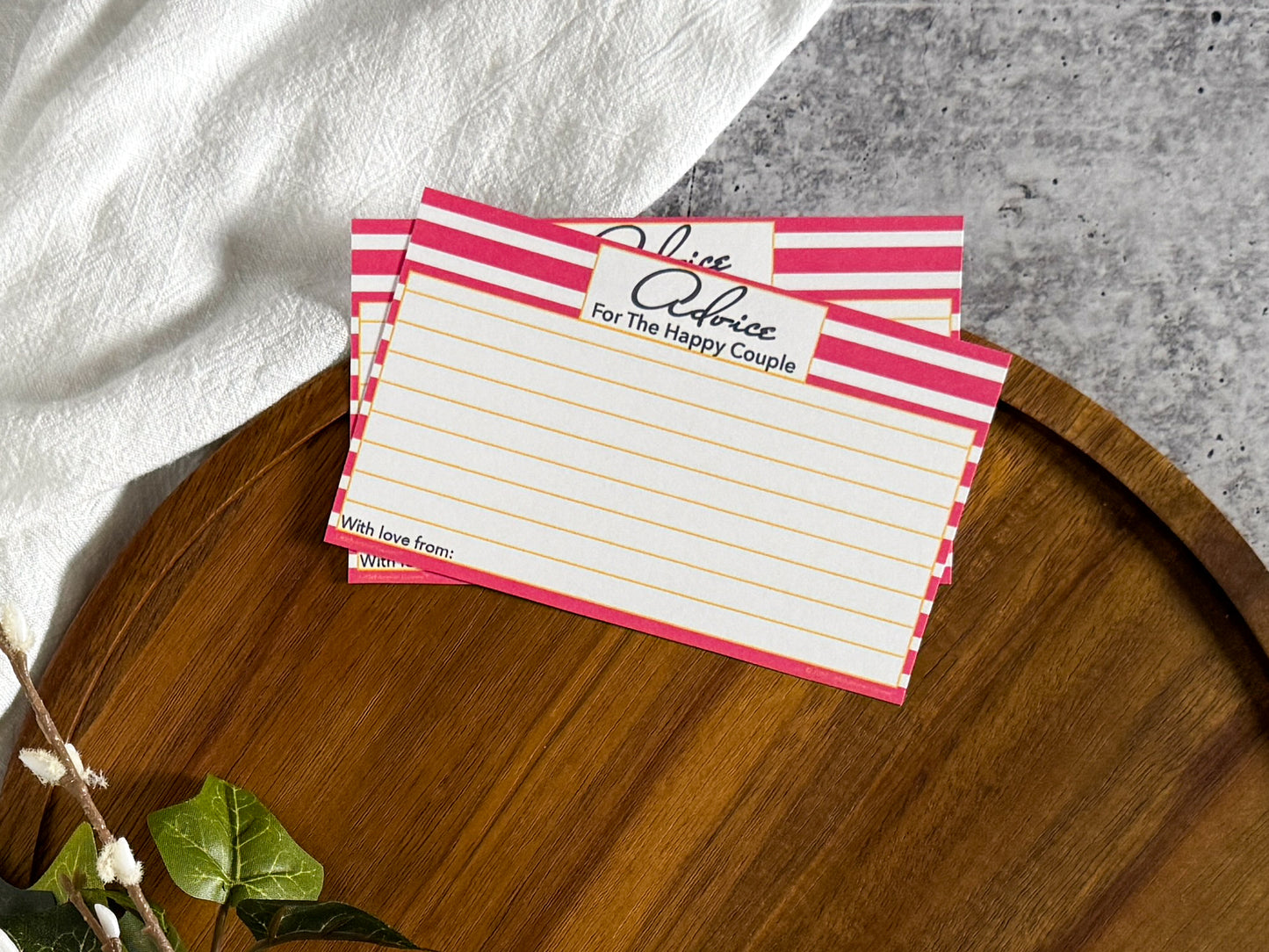 2 Pink Stripe Advice for the Bachelorette cards laying on the top edge of a round wooden tray with a cream cloth and foliage surrounding the tray