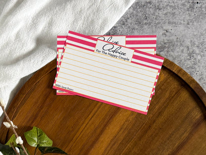 2 Pink Stripe Advice for the Bachelorette cards laying on the top edge of a round wooden tray with a cream cloth and foliage surrounding the tray