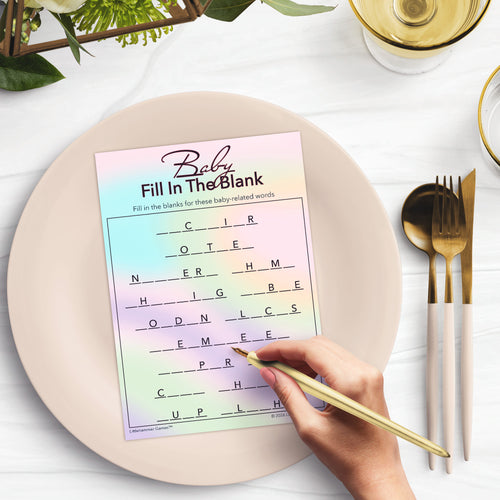 Hologram-themed Baby Fill in the Blank baby shower game card on a plate with a hand holding a pen, surrounded by gold cutlery and greenery.