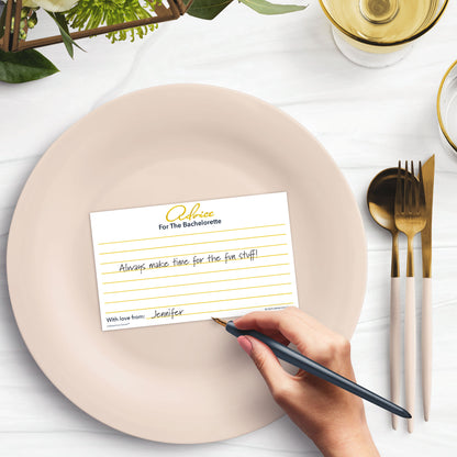 Woman’s hand holding a pen writing advice for the bachelorette on a card at a light place setting