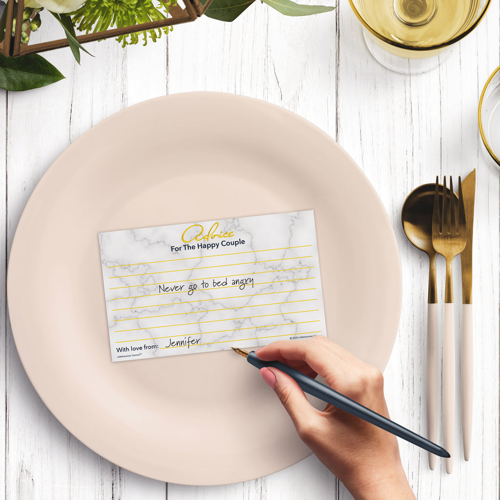 Woman’s hand holding a pen leaving a note on an Advice for the Happy Couple wedding advice card at a light place setting