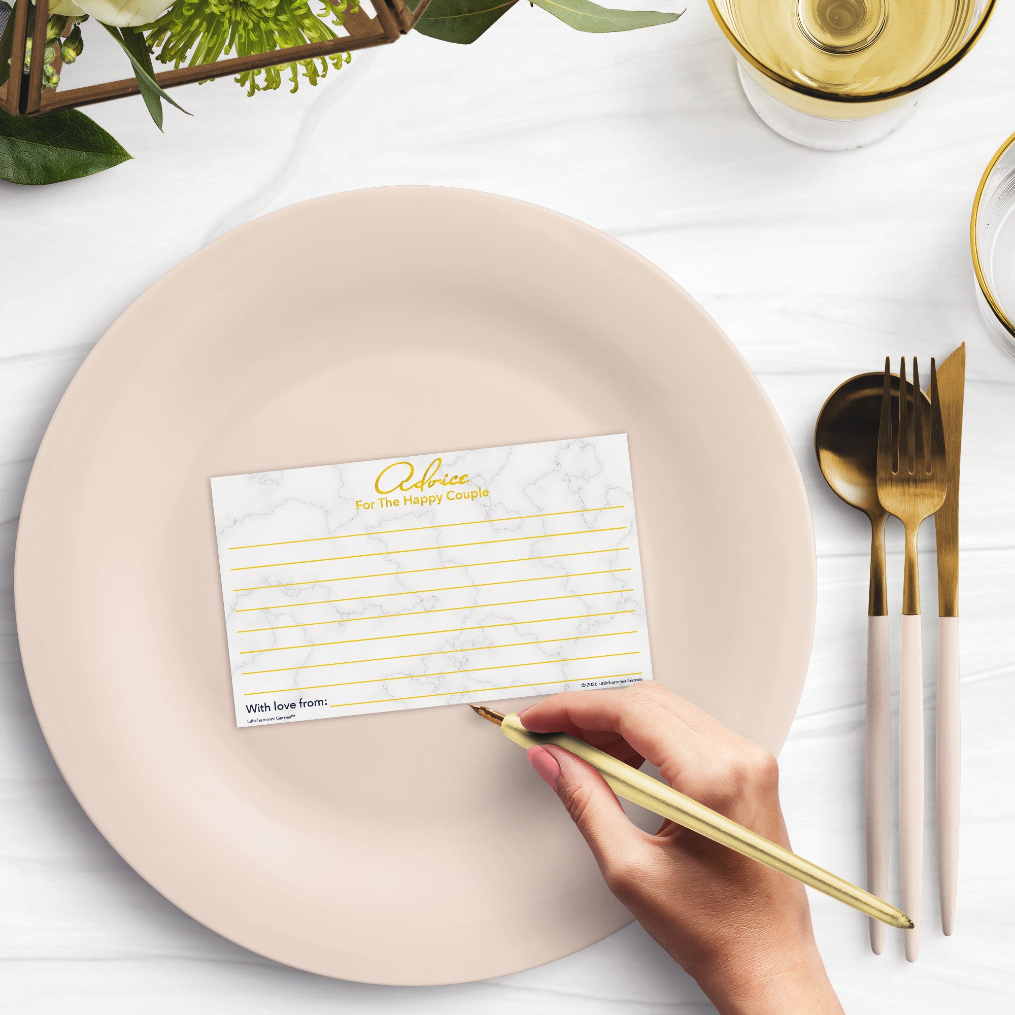 Woman’s hand holding a pen leaving a note on an Advice for the Happy Couple wedding advice card at a light place setting