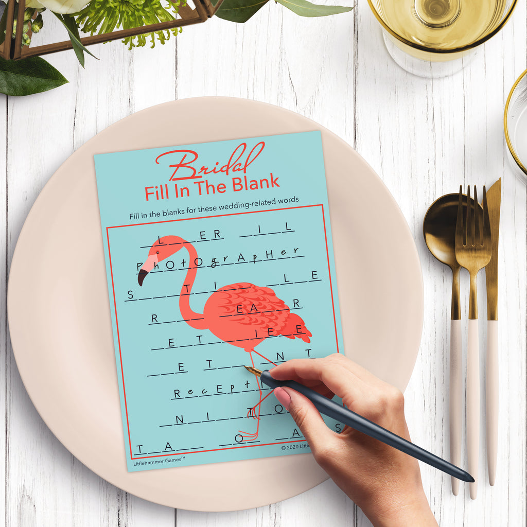 Woman’s hand holding a pen playing a flamingo Bridal Fill in the Blank game card at a light place setting