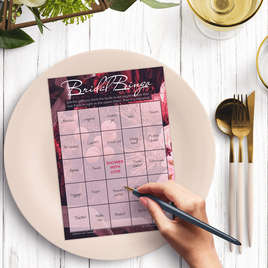 Woman with a pen sitting at a dark place setting with a black and gold plate filling out a floral-themed Bridal Gift Bingo card