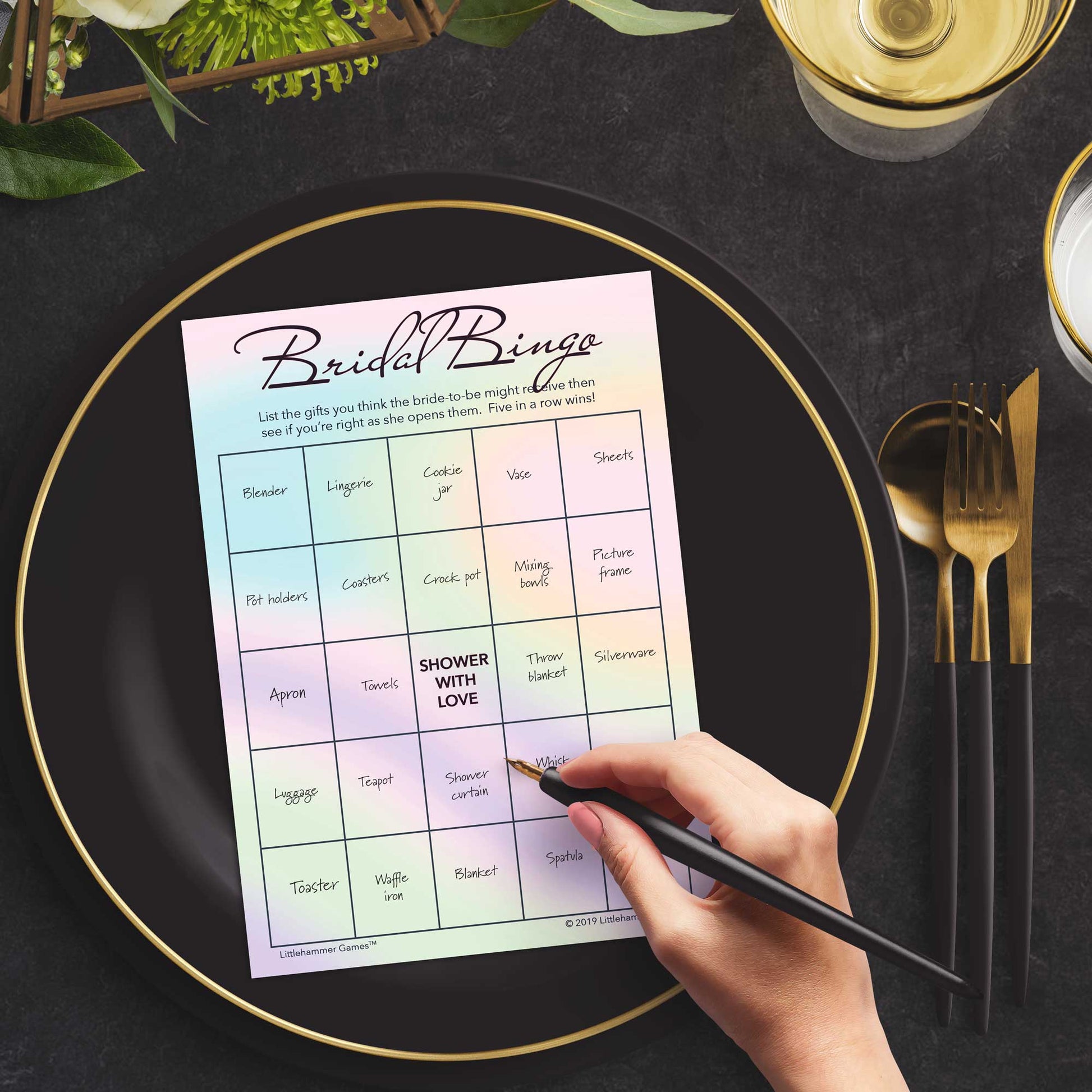 Woman with a pen sitting at a dark place setting with a black and gold plate filling out a hologram-themed Bridal Gift Bingo card