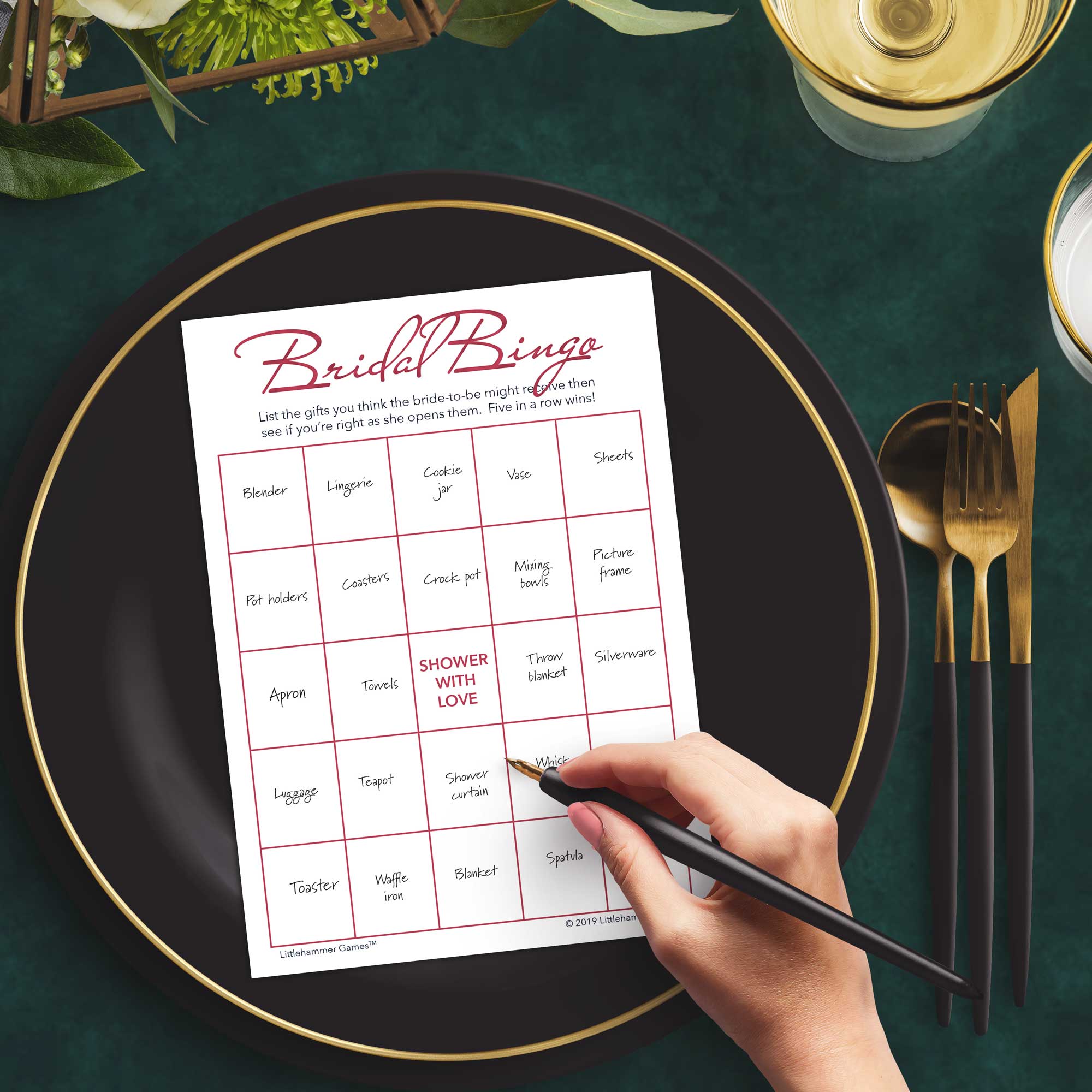 Woman with a pen sitting at a dark place setting with a black and gold plate filling out a rose gold and white Bridal Gift Bingo card