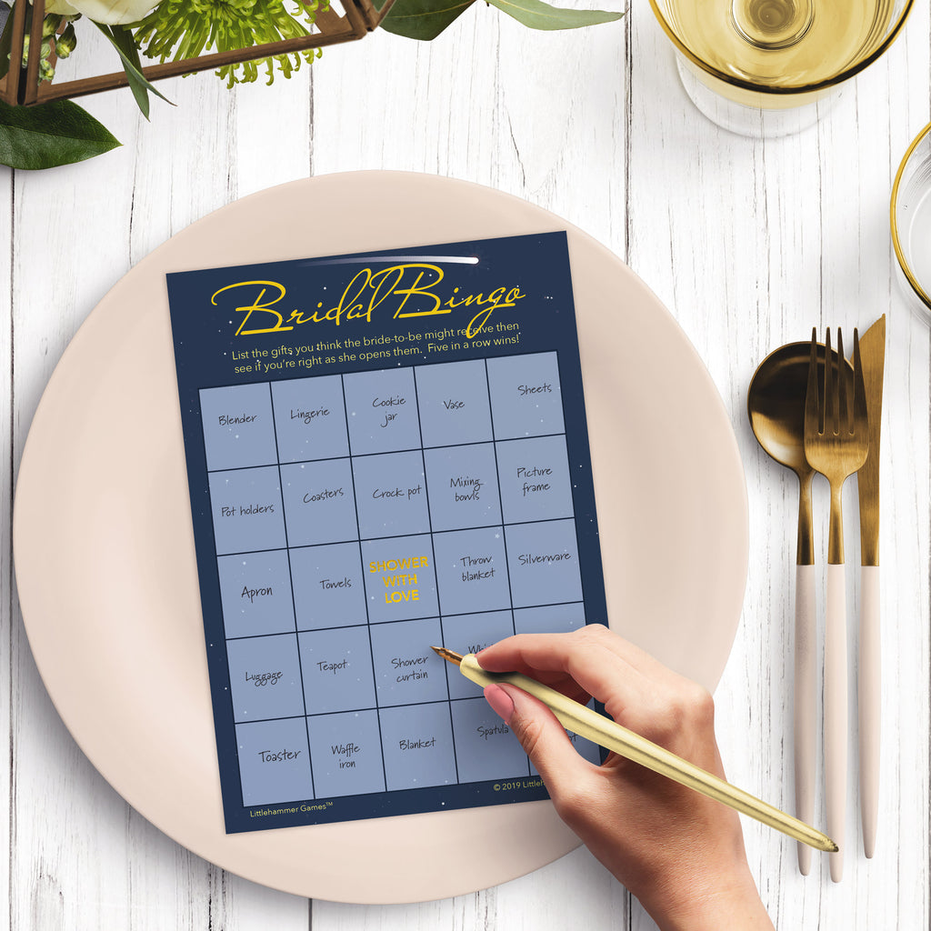 Woman with a pen sitting at a dark place setting with a black and gold plate filling out a celestial-themed Bridal Gift Bingo card