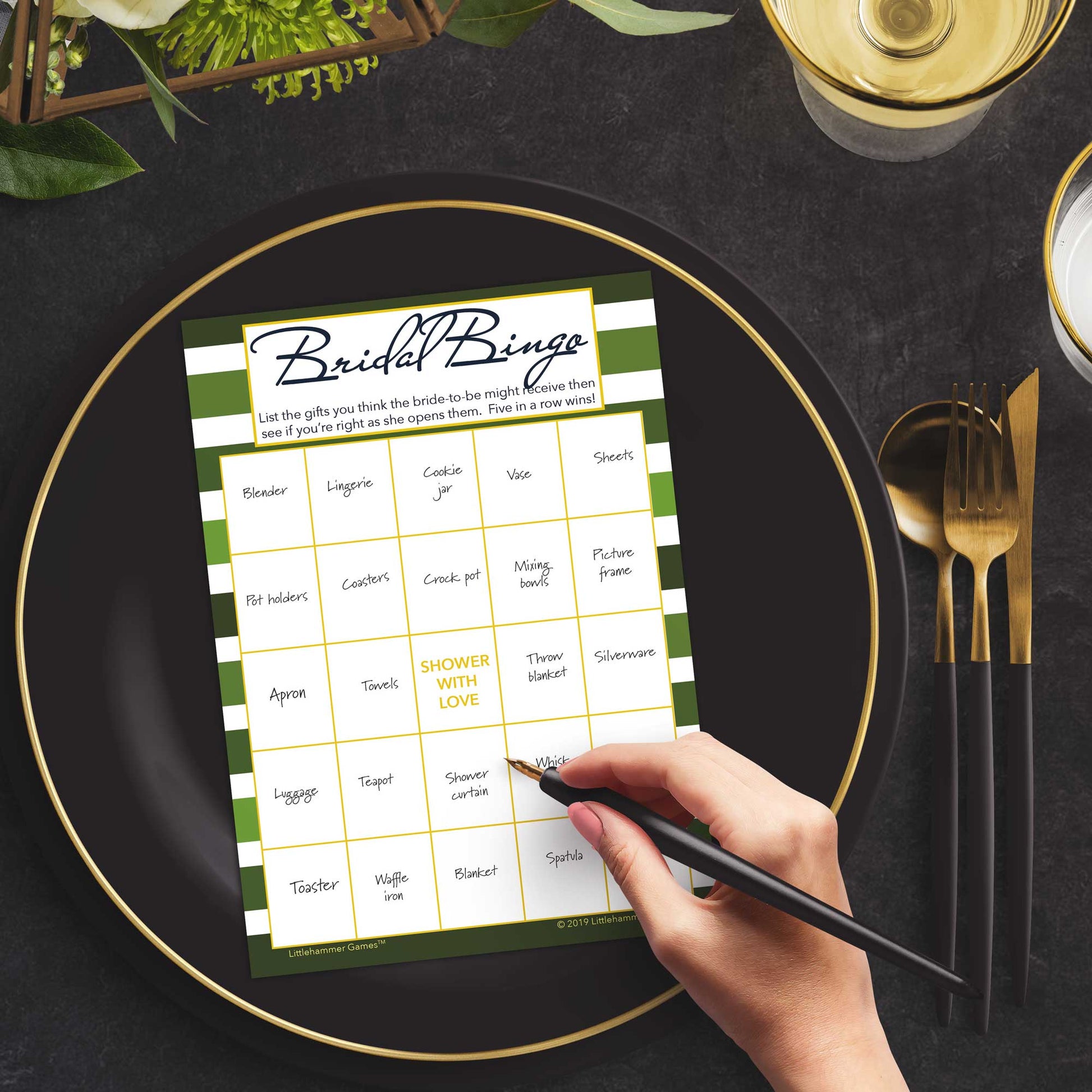 Woman with a pen sitting at a dark place setting with a black and gold plate filling out a green-striped Bridal Gift Bingo card