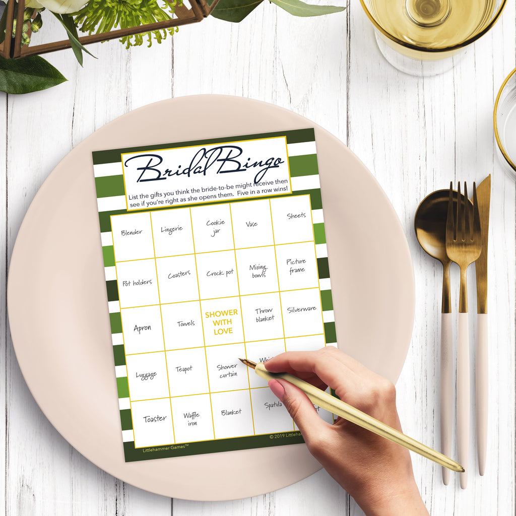 Woman with a pen sitting at a dark place setting with a black and gold plate filling out a green-striped Bridal Gift Bingo card