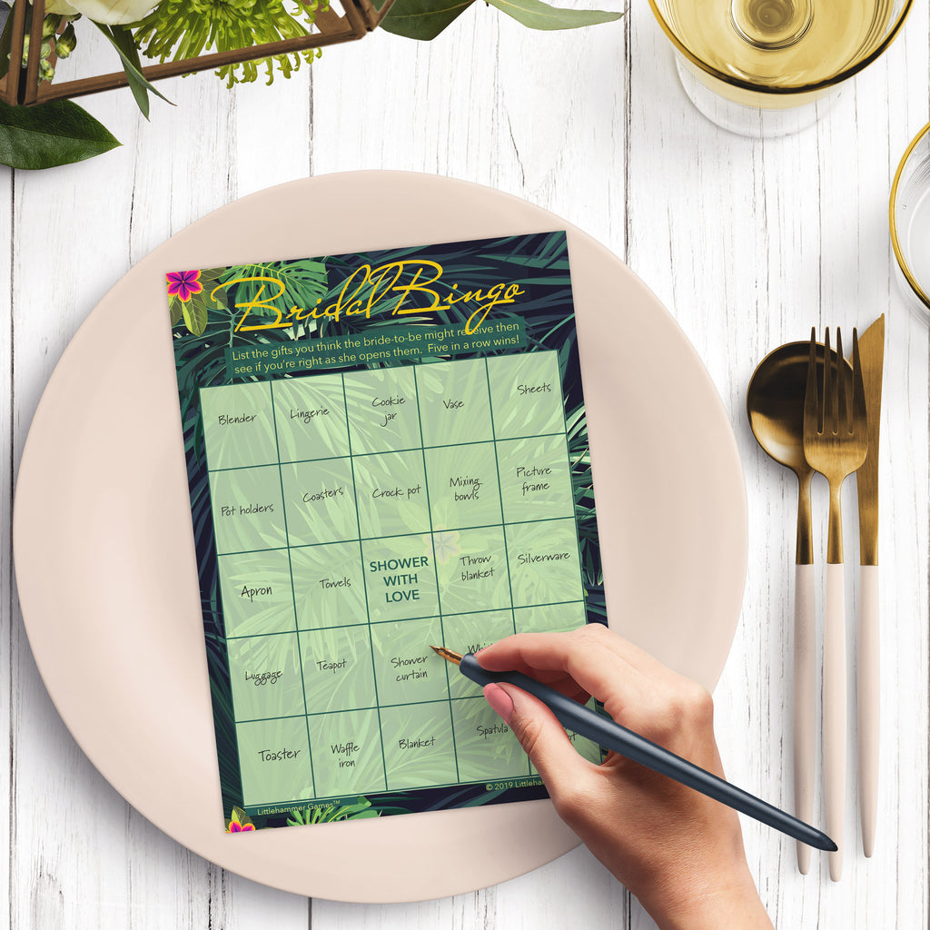 Woman with a pen sitting at a dark place setting with a black and gold plate filling out a tropical-themed Bridal Gift Bingo card