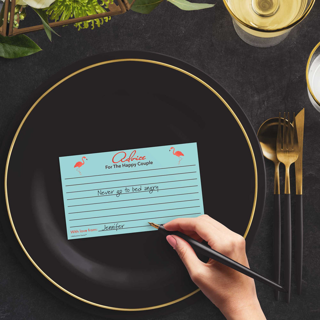 Woman with a pen sitting at a dark place setting with a black and gold plate filling out a flamingo-themed Advice for the Happy Couple card