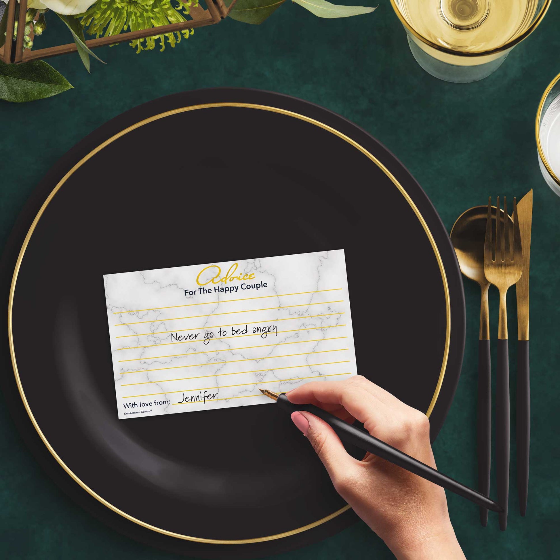 Woman with a pen sitting at a dark place setting with a black and gold plate filling out a gold and marble Advice for the Happy Couple card