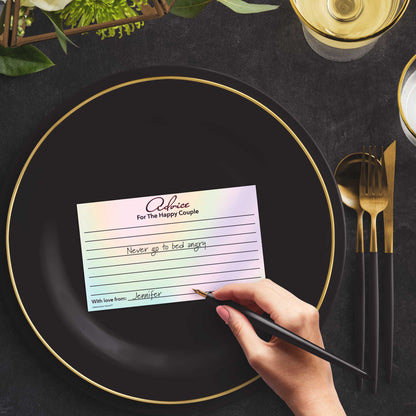 Woman with a pen sitting at a dark place setting with a black and gold plate filling out a hologram-themed Advice for the Happy Couple card