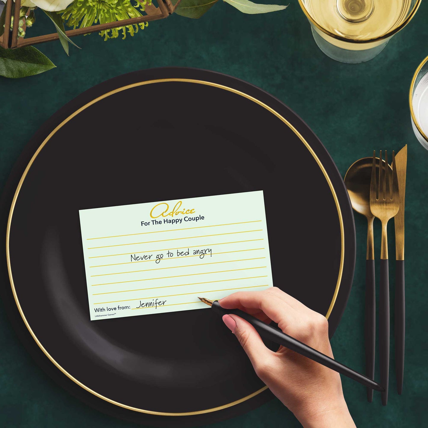 Woman with a pen sitting at a dark place setting with a black and gold plate filling out a mint and gold Advice for the Happy Couple card