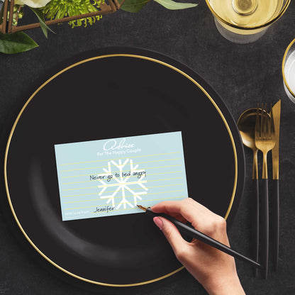Woman with a pen sitting at a dark place setting with a black and gold plate filling out a snowflake-themed Advice for the Happy Couple card