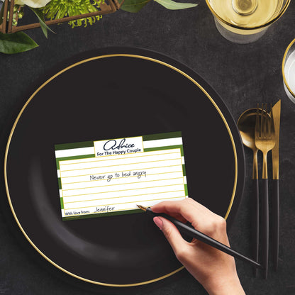 Woman with a pen sitting at a dark place setting with a black and gold plate filling out a green-striped Advice for the Happy Couple card
