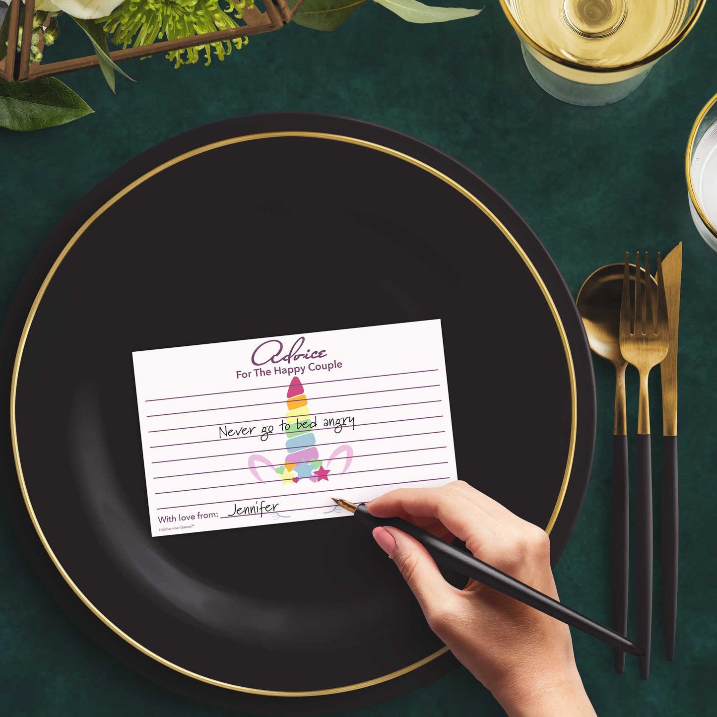 Woman with a pen sitting at a dark place setting with a black and gold plate filling out a unicorn-themed Advice for the Happy Couple card