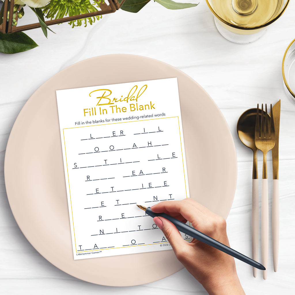 Woman’s hand holding a pen playing a gold and white Bridal Fill in the Blank game card at a light place setting