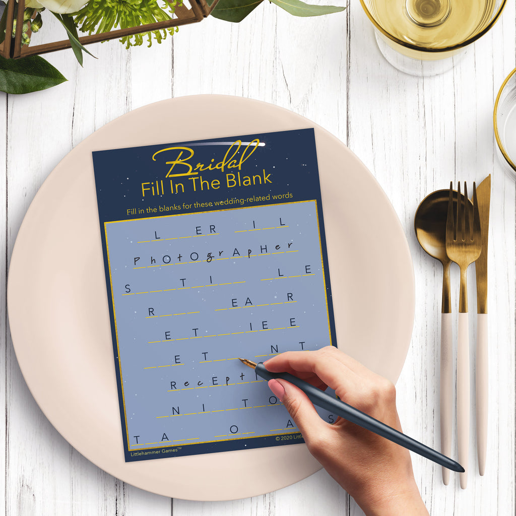 Woman’s hand holding a pen playing a starry night sky Bridal Fill in the Blank game card at a light place setting