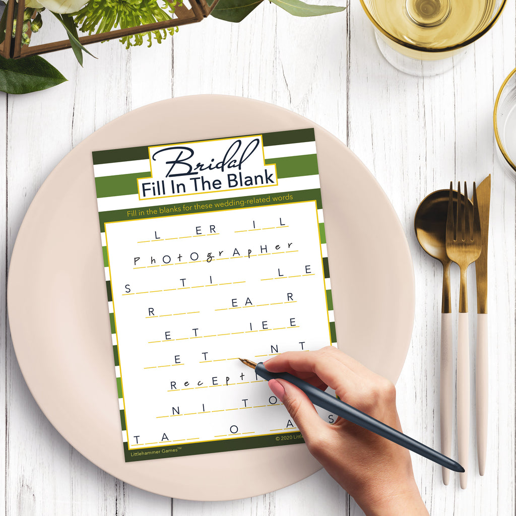 Woman’s hand holding a pen playing a striped green Bridal Fill in the Blank game card at a light place setting
