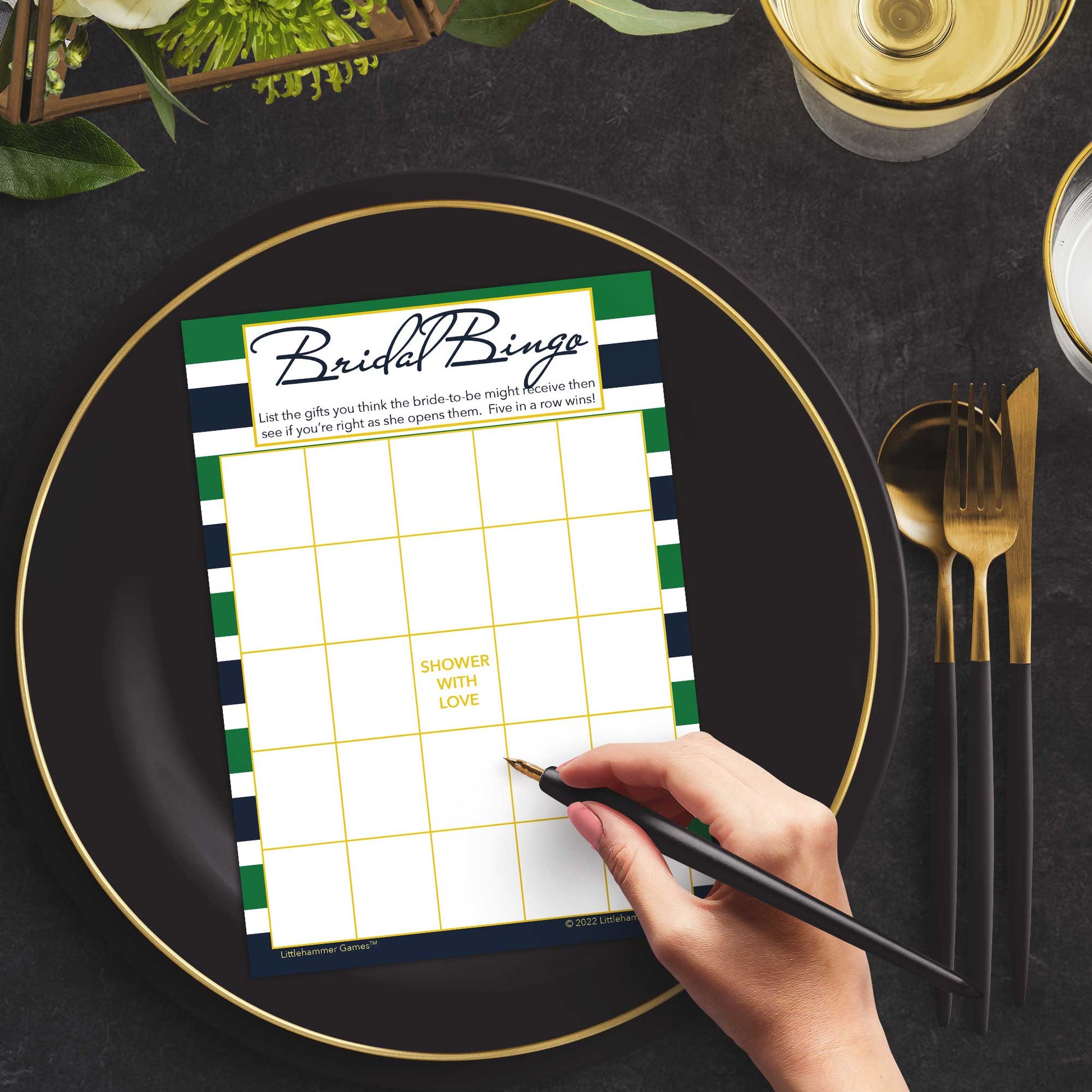 Woman with a pen sitting at a dark place setting with a black and gold plate filling out a green and navy-striped Bridal Gift Bingo card