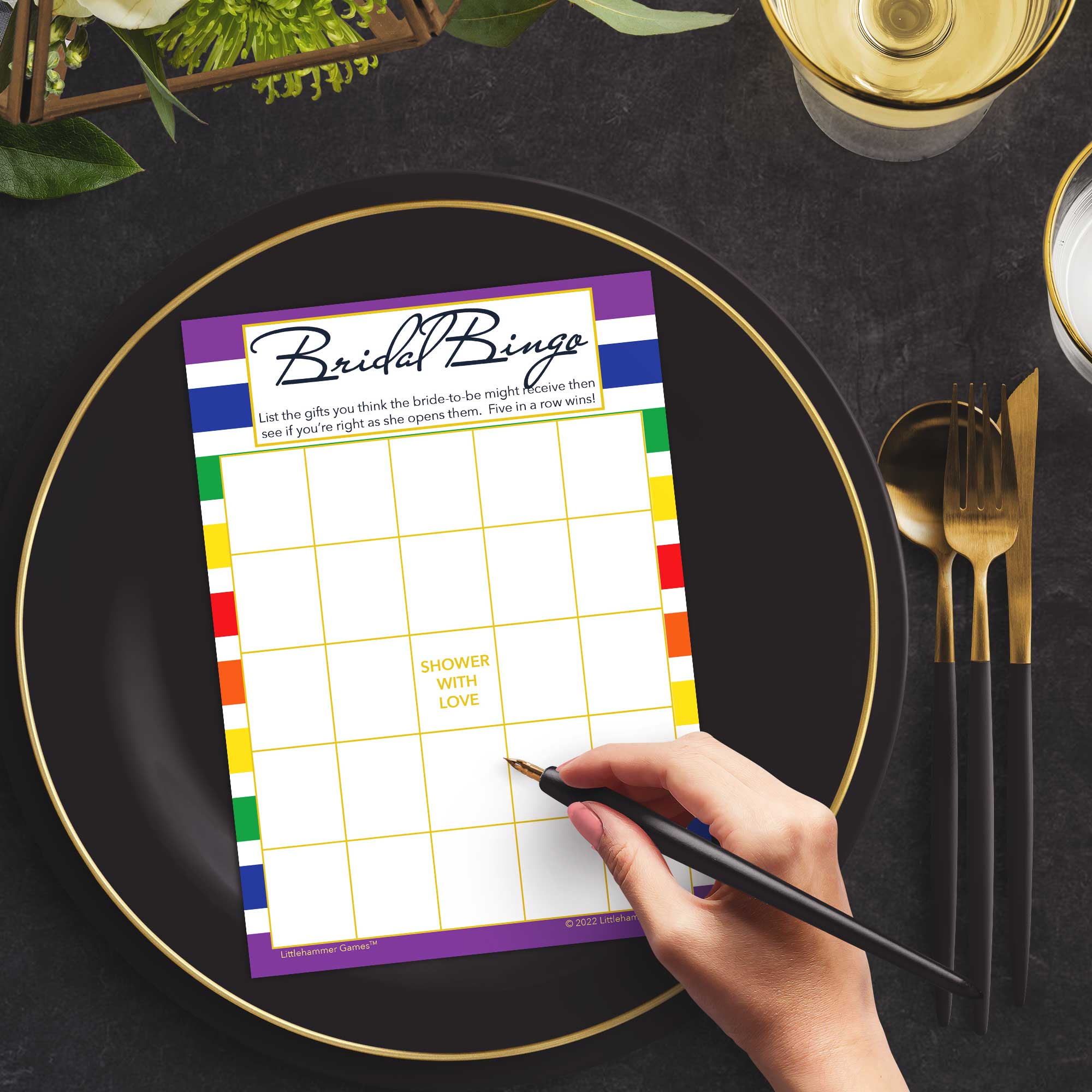 Woman with a pen sitting at a dark place setting with a black and gold plate filling out a rainbow-striped Bridal Gift Bingo card