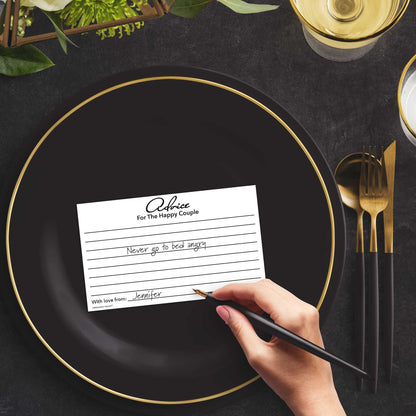 Woman with a pen sitting at a dark place setting with a black and gold plate filling out a black and white Advice for the Happy Couple card