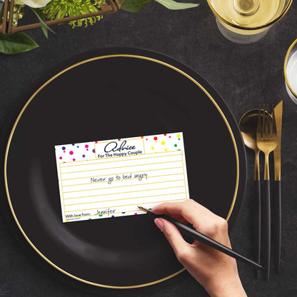 Woman with a pen sitting at a dark place setting with a black and gold plate filling out a rainbow polka dot Advice for the Happy Couple card