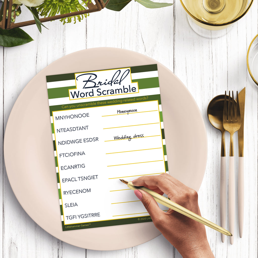 Woman’s hand holding a pen playing a green stripe Bridal Word Scramble game card at a light place setting