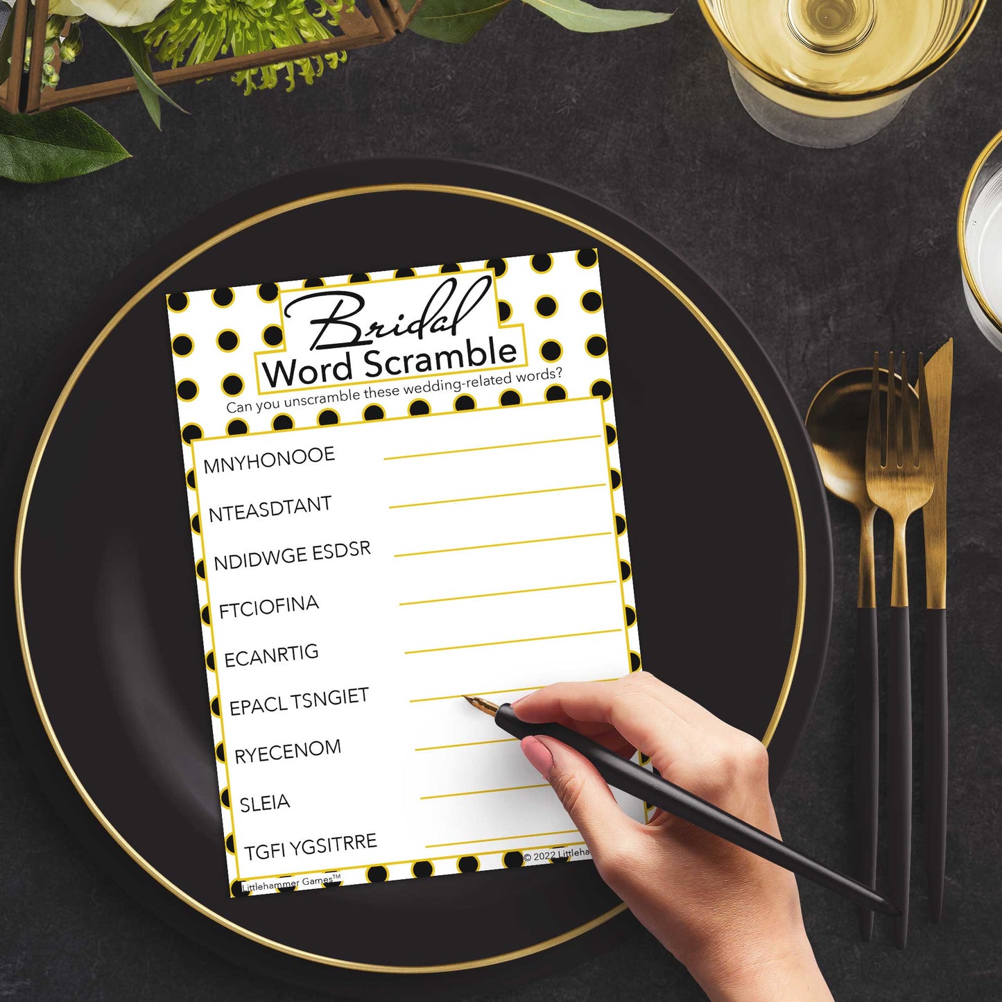 Woman with a pen playing a black and gold polka dot Bridal Word Scramble game card at a dark place setting
