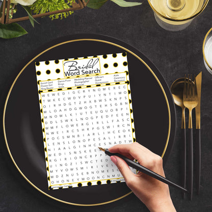 Woman with a pen playing a black and gold polka dot Bridal Word Search game card at a dark place setting