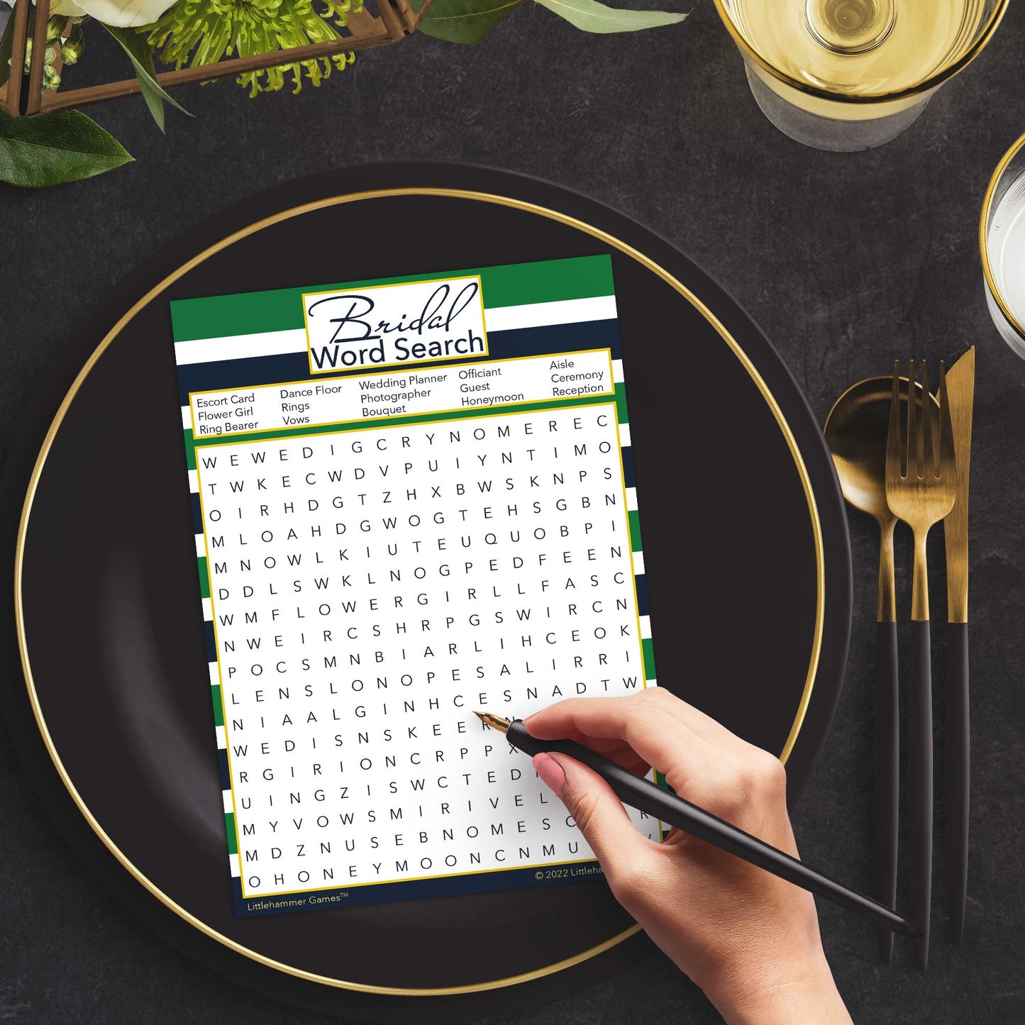 Woman with a pen playing a green and navy-striped Bridal Word Search game card at a dark place setting