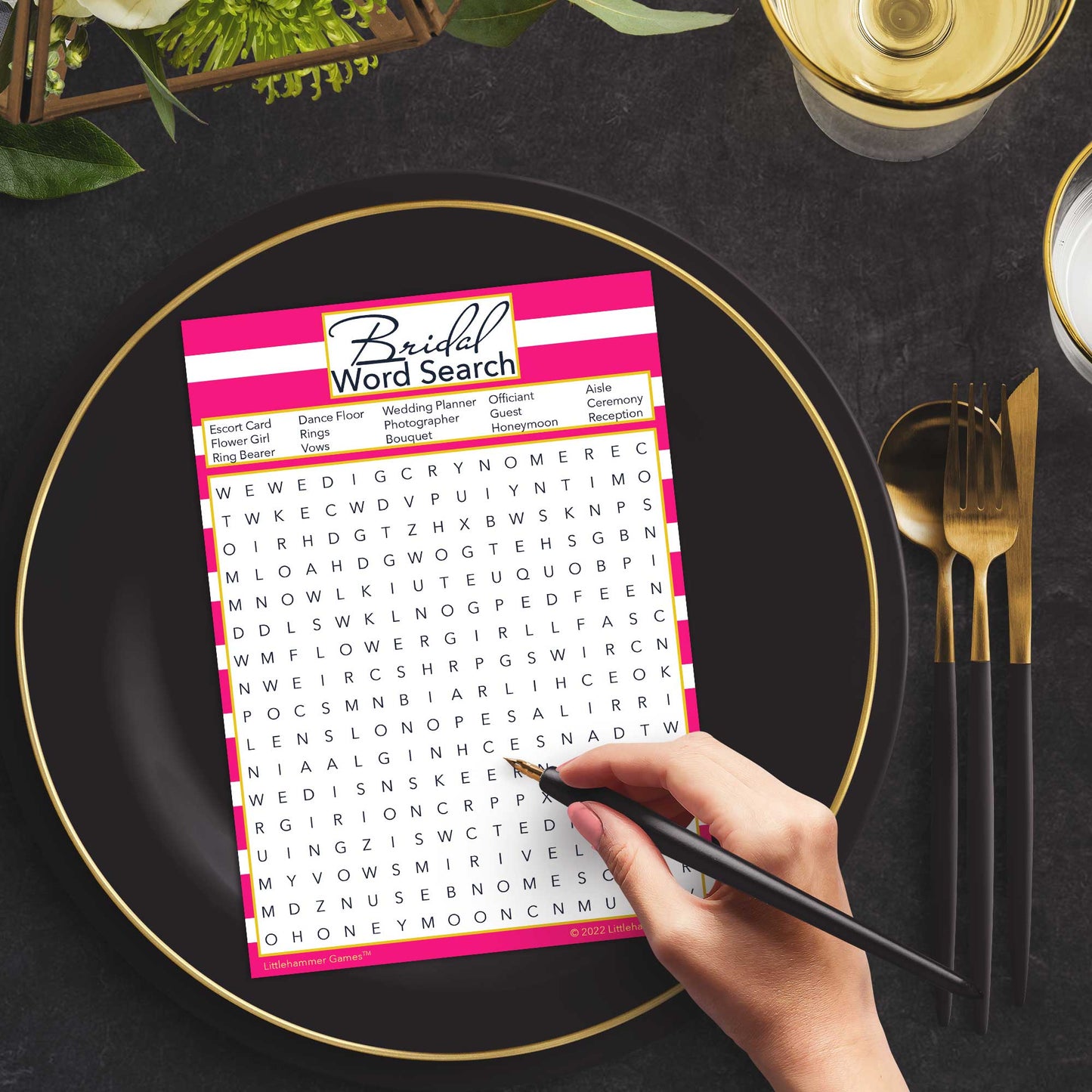 Woman with a pen playing a pink-striped Bridal Word Search game card at a dark place setting