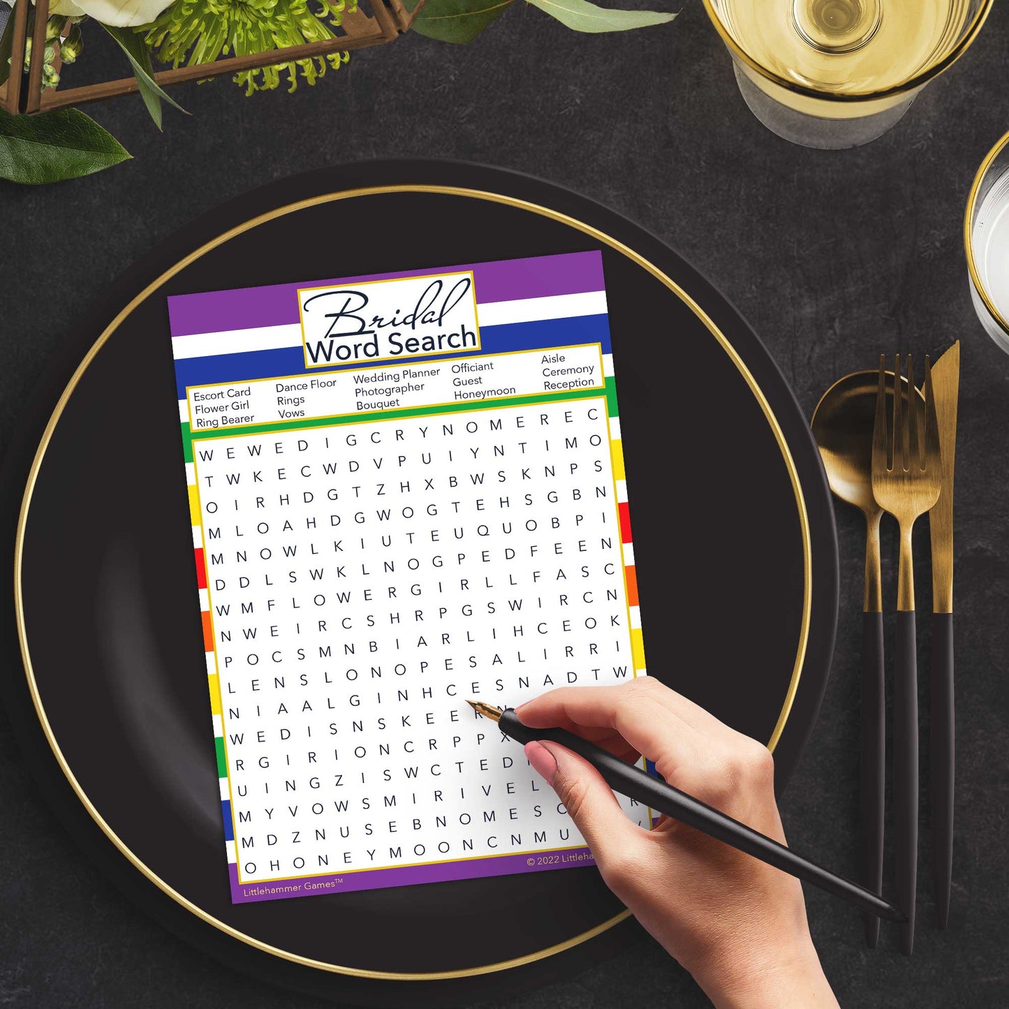 Woman with a pen playing a rainbow-striped Bridal Word Search game card at a dark place setting