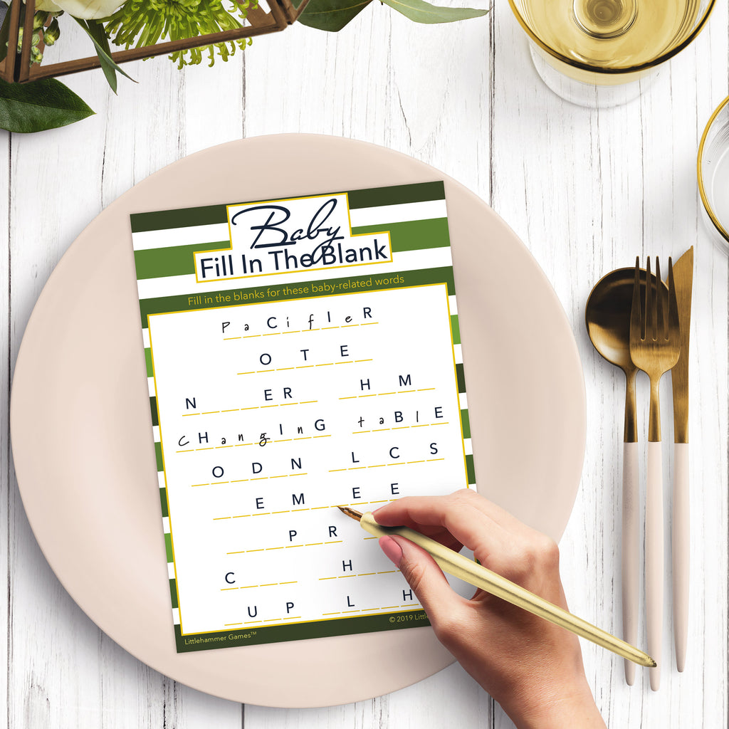 Woman’s hand holding a pen playing a shades of green-striped Baby Fill in the Blank game card at a light place setting