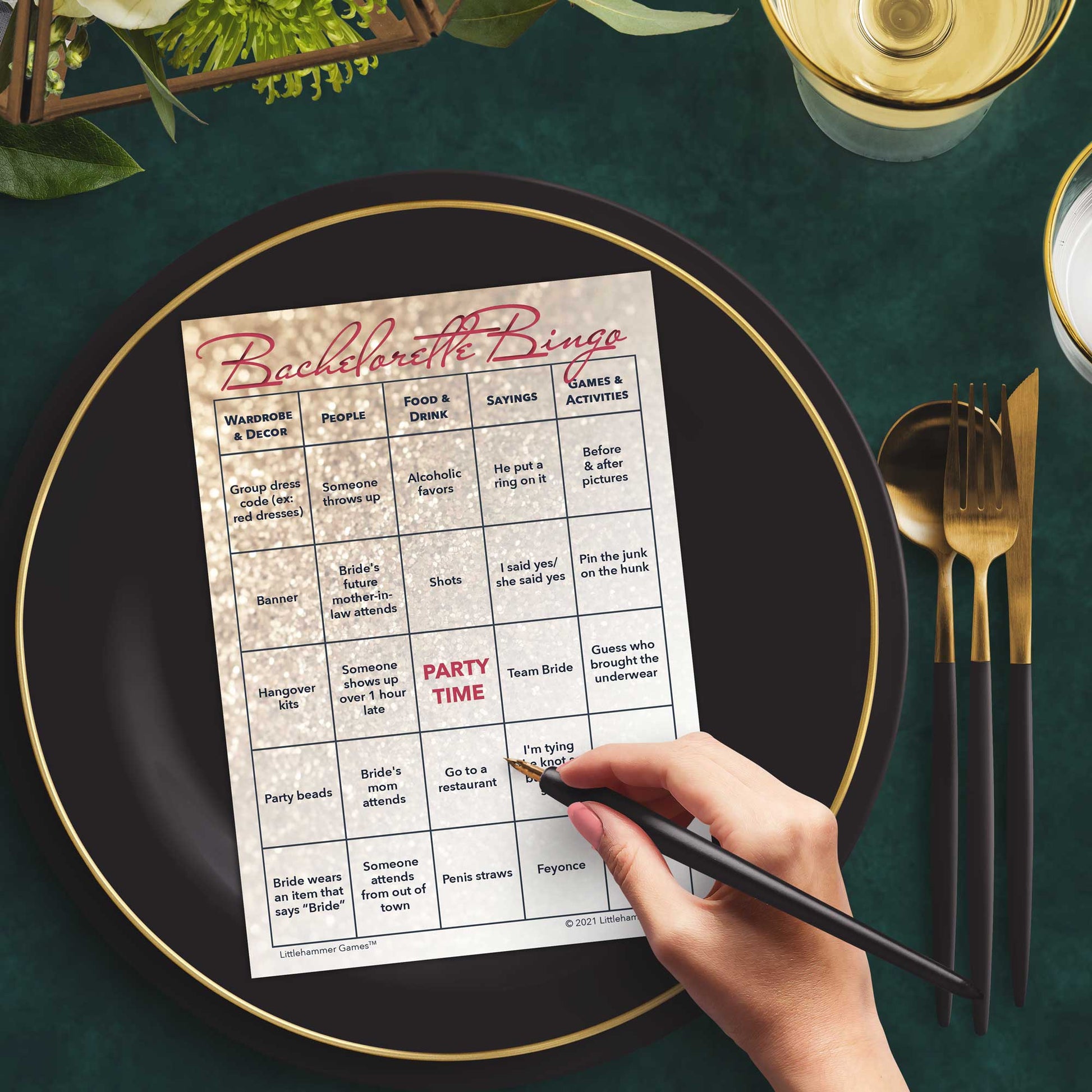 Woman with a pen sitting at a table with a glittery rose gold Bachelorette Bingo game card on a gold and black plate on a dark place setting