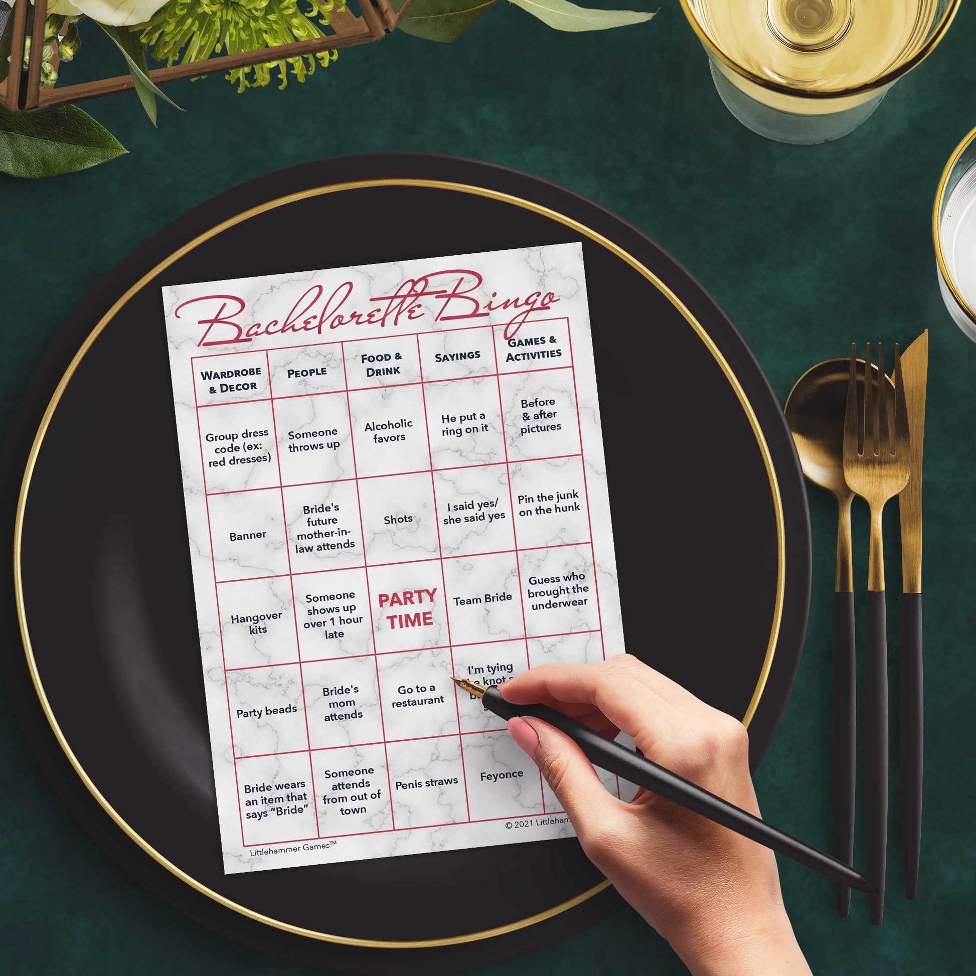Woman with a pen sitting at a table with a rose gold and marble Bachelorette Bingo game card on a gold and black plate on a dark place setting