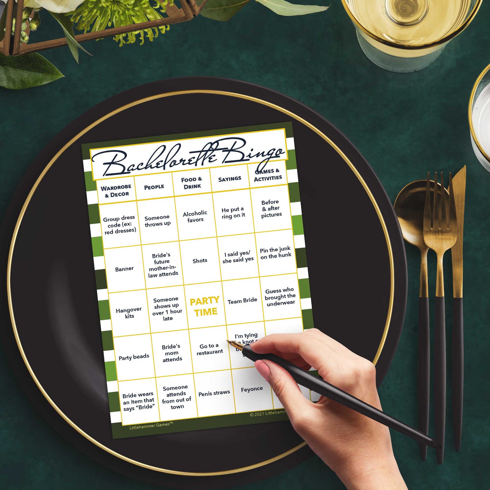 Woman with a pen sitting at a table with a green-striped Bachelorette Bingo game card on a gold and black plate on a dark place setting