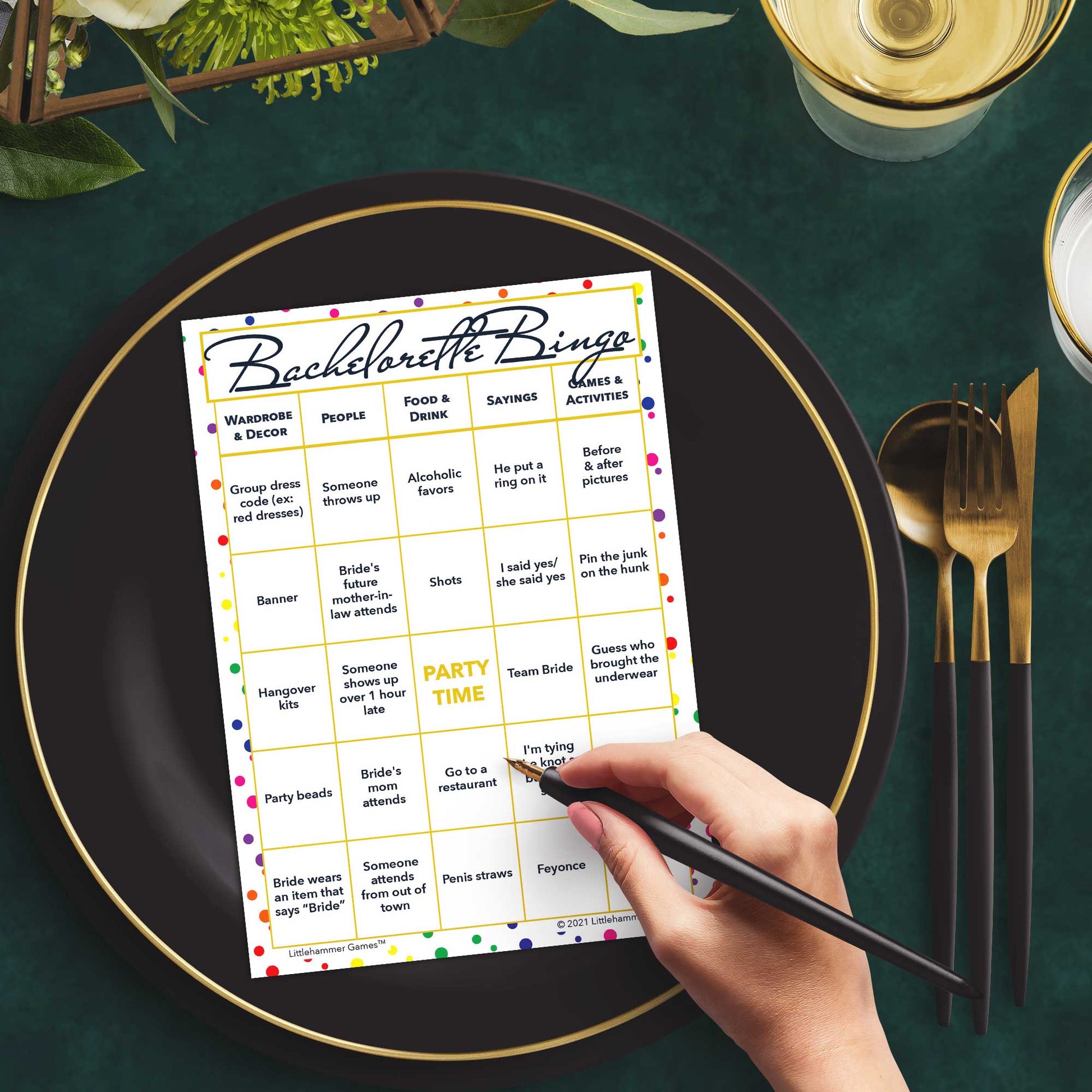 Woman with a pen sitting at a table with a rainbow polka dot Bachelorette Bingo game card on a gold and black plate on a dark place setting